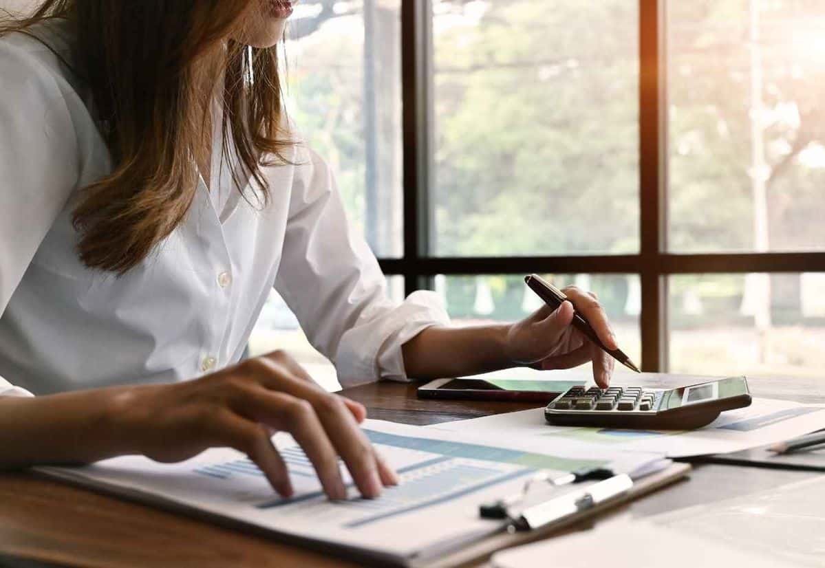 Persona analizando documentos financieros y utilizando una calculadora en una oficina iluminada, representando la revisión detallada de contratos para evitar tasas ocultas en los préstamos.